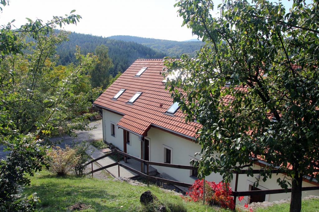 Vidiecky dom s červenou strechou obklopený bujnou zeleňou.